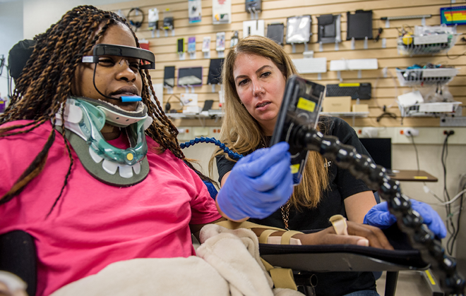 Patient with a neck brace using a wheelchair and assistive technology tools in conjunction with speech therapy